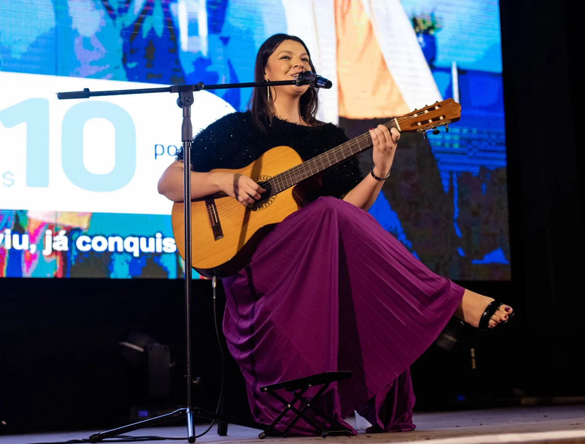 Mari Carvalho no palco, com violão, abrindo o evento